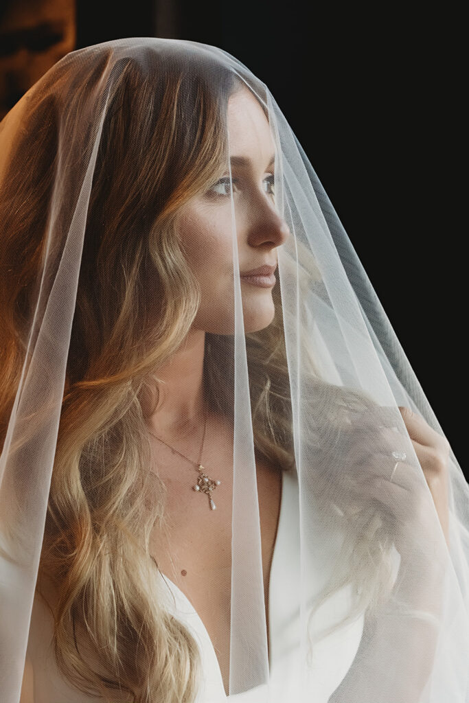 Bride looking out window with wedding hair and makeup complete by luxury Park City beauty team